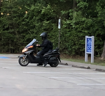 Photo taken of robbery suspect in parking lot wearing all black atop a black power scooter-type motorcycle. 